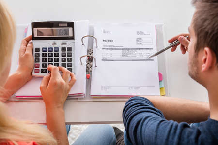 Close-up Of Couple Calculating Family Budget, Invoices, Insurance And Tax Using Calculator At Home