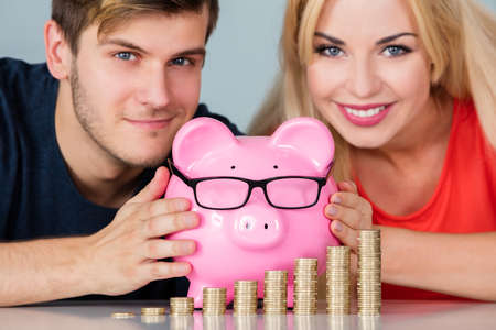 Young Smiling Couple Smart Saving Money In Piggybank With Glasses For 401K Pensionの写真素材