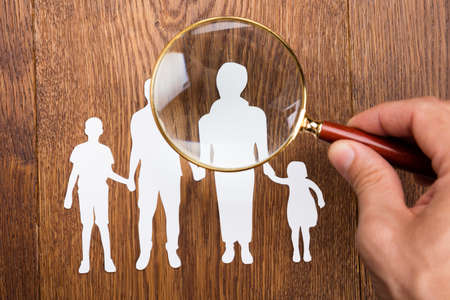 High Angle View Of Person Using Magnifying Glass On Family Papercut At Wooden Deskの写真素材