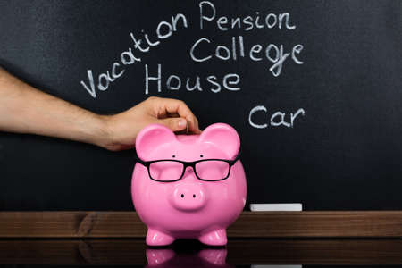 Person Hand Inserting Coin In Piggybank For Daily Expenses In Front Of Blackboardの写真素材