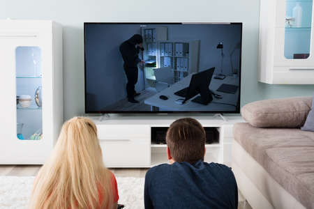 Young Couple Lying On Carpet Watching Suspense Movie On Television At Homeの写真素材