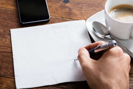 High Angle View Of Person Hand Holding Pen On Blank White Paper On Wooden Deskの写真素材
