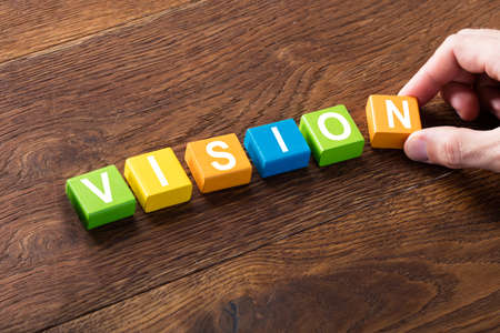 High Angle View Of A Person Arranging Block Of Vision Letter On Wooden Desk