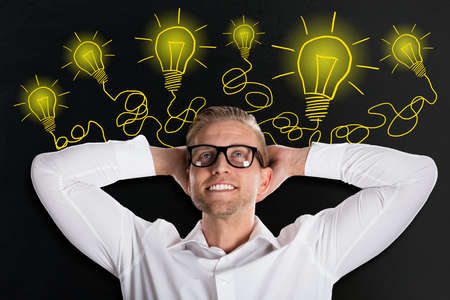 Handsome Smiling Young Man Looking Up With Creative Light Bulb Sketches On Blackboardの写真素材