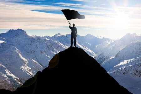 Silhouette Of A Man Standing On Top Of The Mountain Peak Waving Flagの写真素材