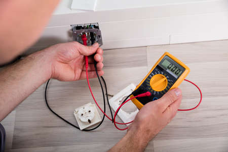 Close-up Of Person's Hand Holding Multimeter Checking Socket Voltage In A Wall Fixtureの写真素材