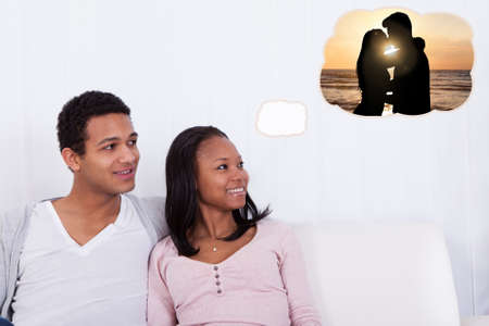Young African Couple Sitting On Sofa Dreaming Of Spending Romantic Vacation With Each Otherの写真素材