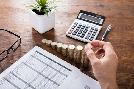 Person Stacking Coins With Calculator On Wooden Desk. Investment And Insurance Conceptの写真素材
