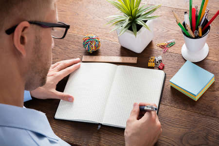 High Angle View Of A Person Writing Note In Blank Diary On Wooden Deskの写真素材