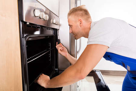 Young Male Technician Repairing Oven In Kitchenの写真素材