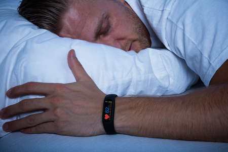 Fitness Activity Tracker With Heartbeat Rate On Man's Hand Over Bedの写真素材