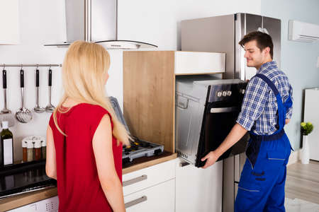 Male Worker Installing Oven For Repairing While Young Woman Standing In Kitchenの写真素材