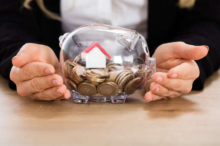Businesswoman Protecting Her Savings With House Model In A Piggybank. Property Investment Conceptの写真素材