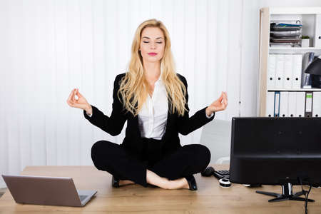 A Young Woman Doing Yoga While Sitting On Wooden Deskの写真素材