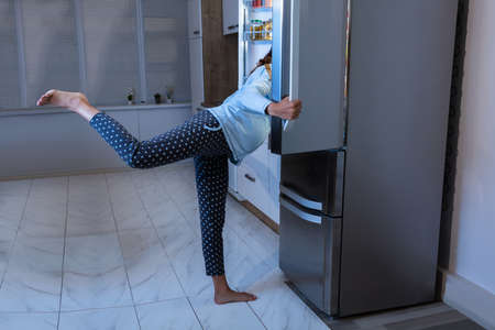 Young Pregnant Woman Looking For Food In Open Refrigeratorの写真素材