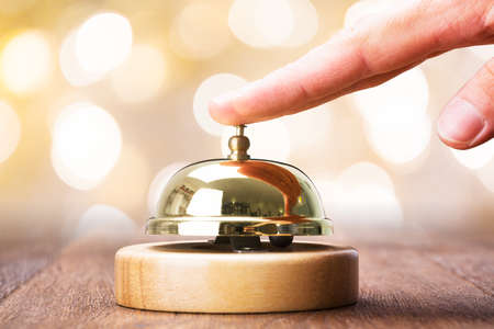 Close-up Of Person Ringing Service Bell On Wooden Deskの写真素材