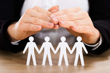 Close-up Of A Businesswoman Protecting Cutout Of Human Figure On Wooden Deskの写真素材