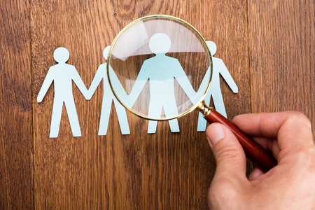 High Angle View Of Person Using Magnifying Glass On Papercut At Wooden Deskの写真素材