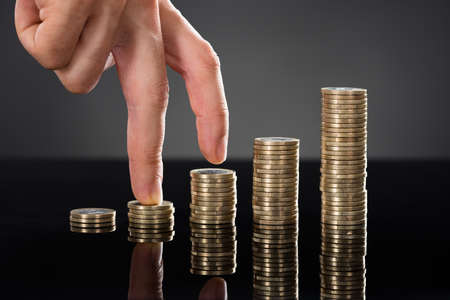 Close-up Of A Person Finger Walking Up Over Stack Of Coins Over Gray Background. Business Growth Conceptの写真素材