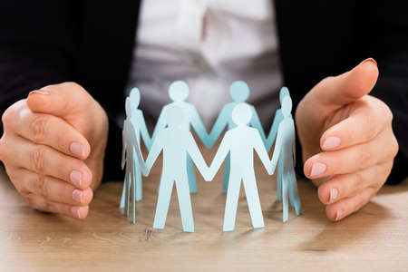 Close-up Of Businesswoman Hand Protecting Cut-out Figures On Desk In Officeの写真素材