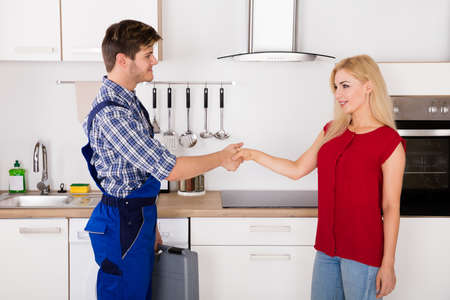 Young Male Repairman Shaking Hands With Young Happy Woman In Kitchenの写真素材