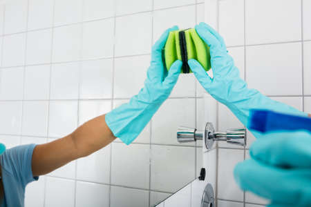 Close-up Of Person Hand Cleaning The Mirror Of The Bathroom Using Sponge At Homeの写真素材