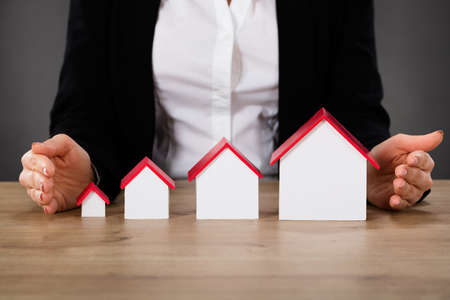 Businesswoman Protecting Different Size Houses In Row On Wooden Table. Property Growth Conceptの写真素材