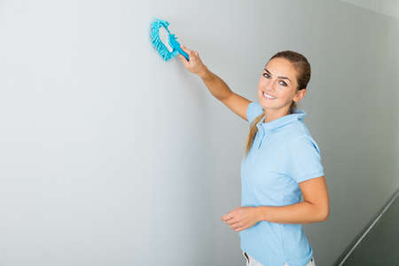 Young Woman Cleaning The Ceiling With Mop On The Corridor Of The Buildingの写真素材