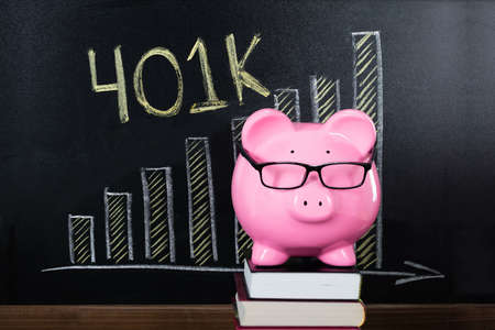 Close-up Of Piggybank Placed On Stacked Book In Front Of Blackboard Showing Graphの写真素材