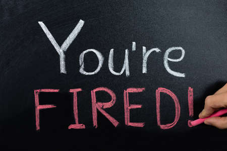 Close-up Of A Person Hand With Fired Concept Written On Blackboardの写真素材