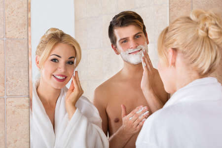 Portrait Of A Man Shaving And Her Wife Cleaning Her Face In Mirror At Bathroomの写真素材