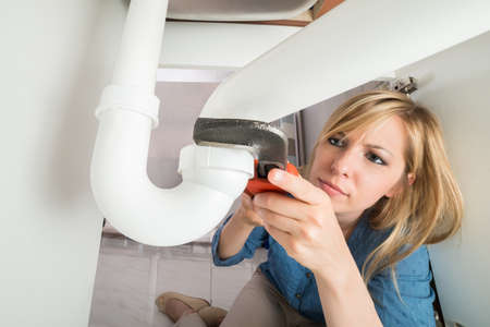 Close-up Of Young Woman Tightening Sink Pipe With Monkey Wrench In Kitchenの写真素材