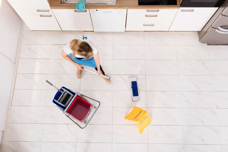 High Angle View Of Young Housemaid Mopping Floor In Kitchenの写真素材