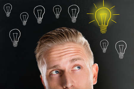 Handsome Thinking Young Man Looking Up With Creative Light Bulb Sketches On Black Boardの写真素材