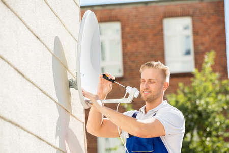 Smiling Young Man Installing TV Satellite Dish To Wallの写真素材