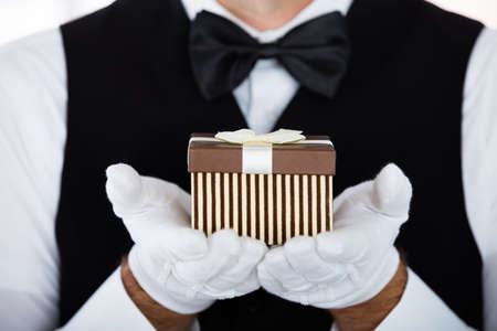 Man Waiter Wearing Bowtie Presenting Small Giftの写真素材