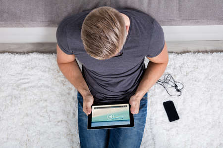 Elevated View Of A Man Sitting On Carpet Watching Video On Digital Tabletの写真素材