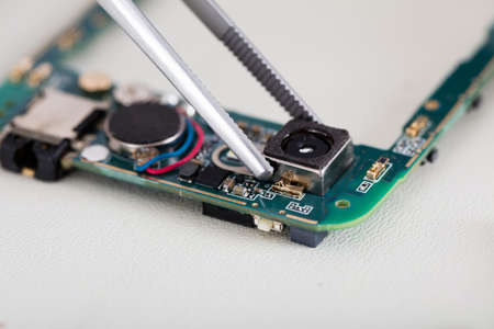 Close-up Of Tweezers On Mobile Phone Changing Broken Cameraの写真素材