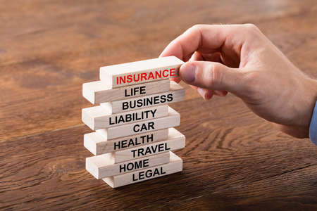 Close-up Of A Person Arranging Stack Of Insurance Concept On Wooden Blockの写真素材