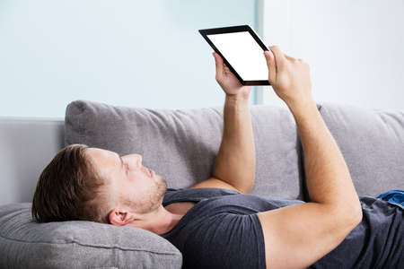 Man Lying On The Couch Looking At Blank Screen On Digital Tabletの写真素材