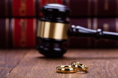 Close-up Of Wedding Rings With Gavel On Wooden Desk In Courtroomの写真素材