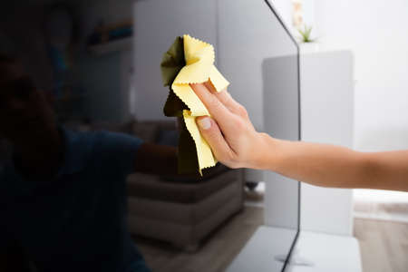 Close-up Of Woman Using Cloth To Clean The Television At Homeの写真素材