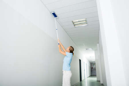 Young Woman Cleaning The Ceiling With Mop On The Corridor Of The Buildingの写真素材