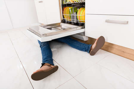 Close-up Of Young Woman Leg Lying Under A Dishwasher In Kitchenの写真素材
