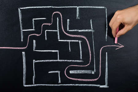 Close-up Of A Person Hand Solving Maze Drawn On Blackboardの写真素材