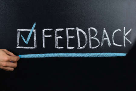 Close-up Of Person Hand Showing Feedback Concept Written On Blackboardの写真素材