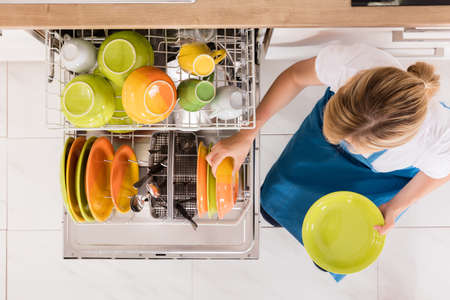 High Angle View Of Young Woman Arranging Plates In Dishwasher At Homeの写真素材