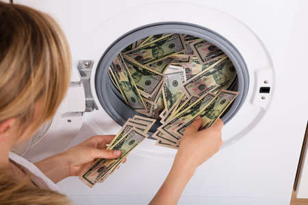 Close-up Of Person Hand Inserting Dirty Money In Washing Machineの写真素材