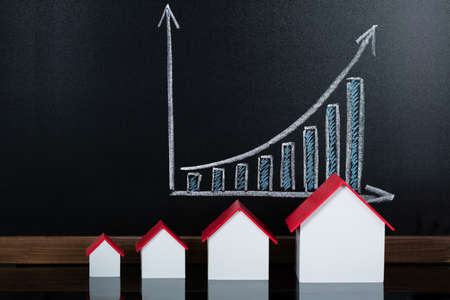 Different Size Of House Models In Front Of Blackboard Showing Business Graphの写真素材
