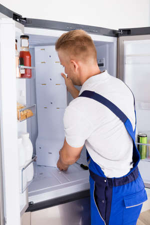 Young Male Repairman Fixing Refrigerator In Kitchenの写真素材